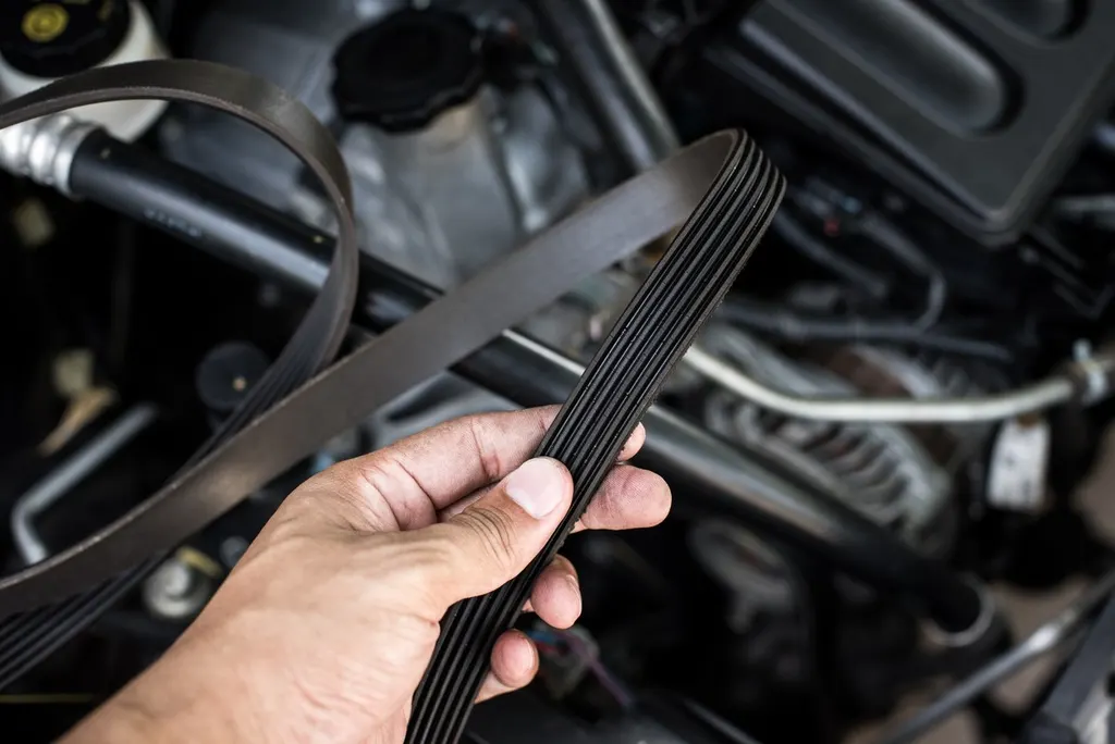 Mechanic holding a worn serpentine belt over an engine